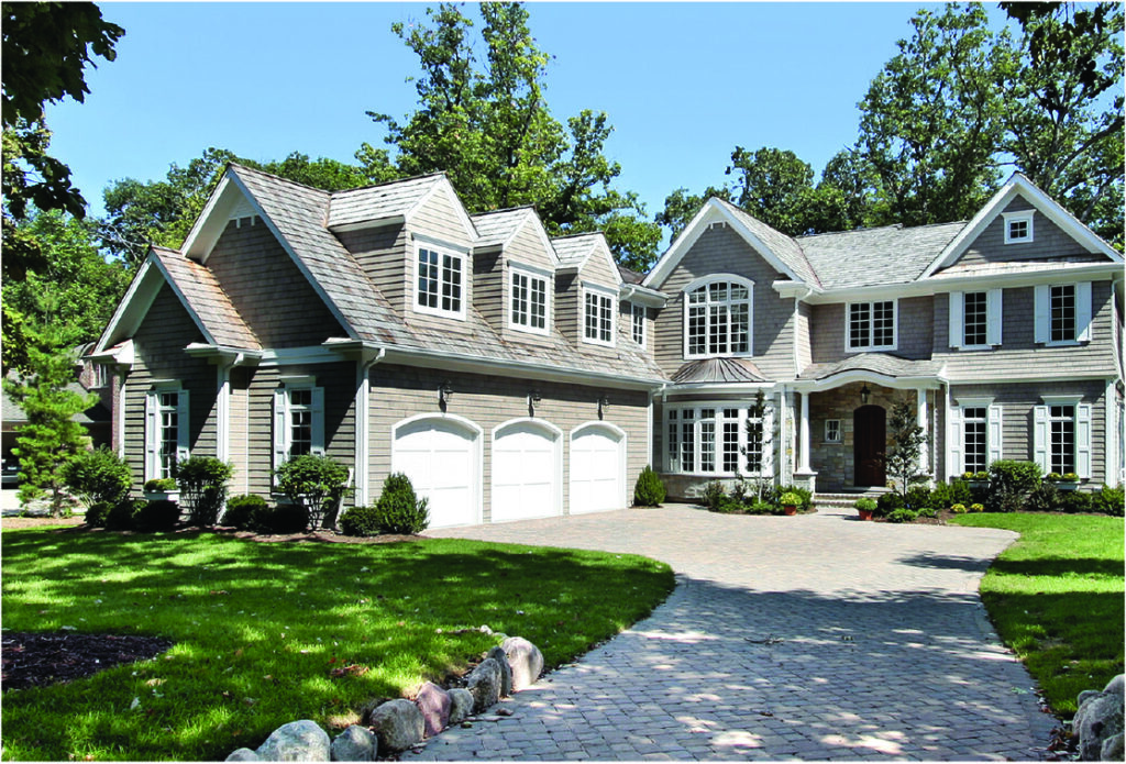 Large shingle-style luxury home with three-car garage, multiple dormers, and stone landscaping.