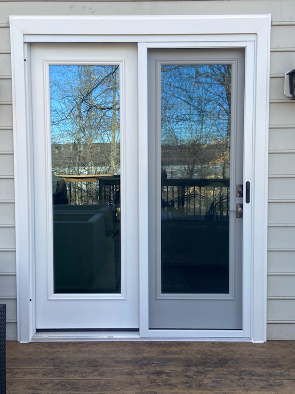 White two-panel sliding patio door on a gray-sided home opening onto a deck.